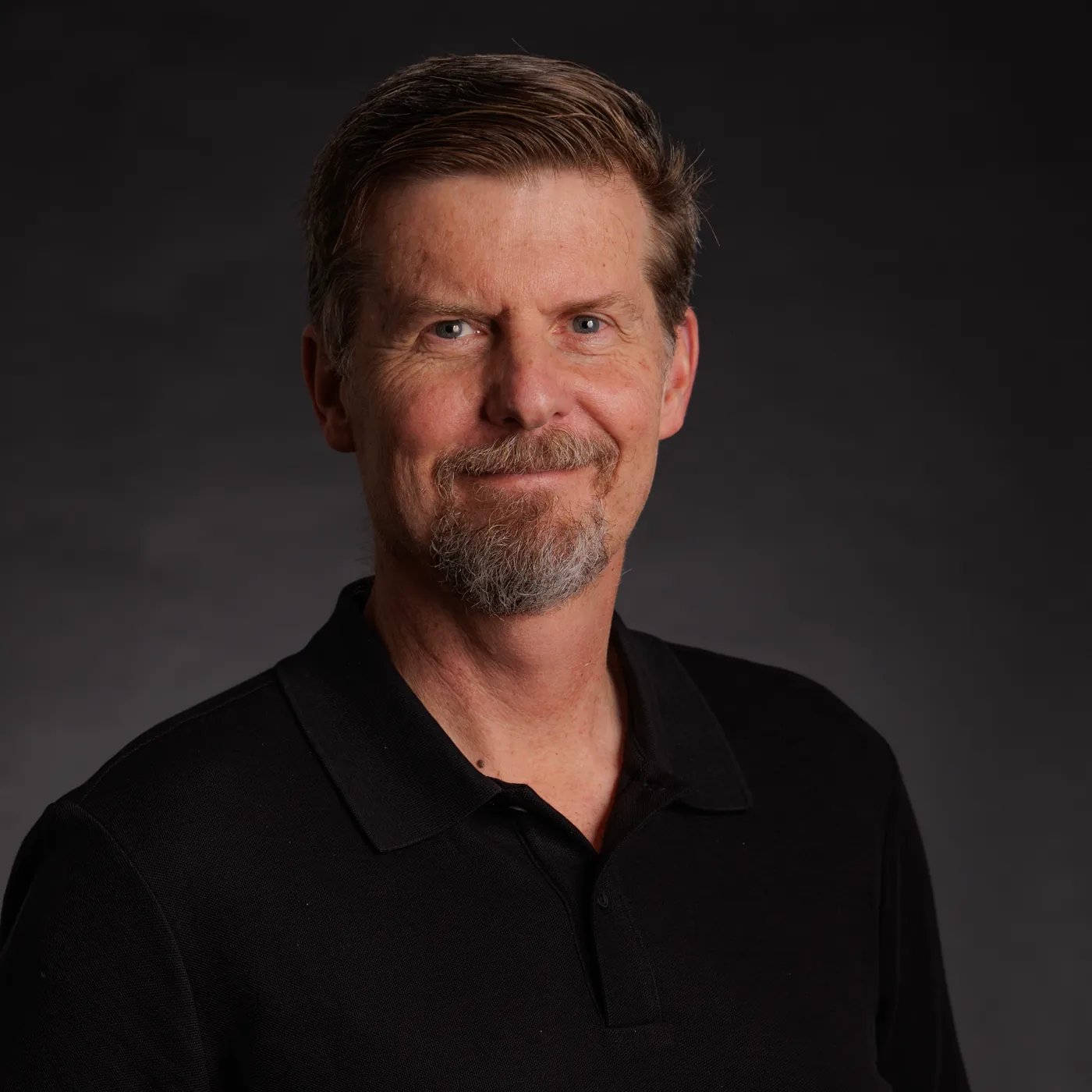 Stuart McClure, smiling, in a black polo shirt against a charcoal studio backdrop.
